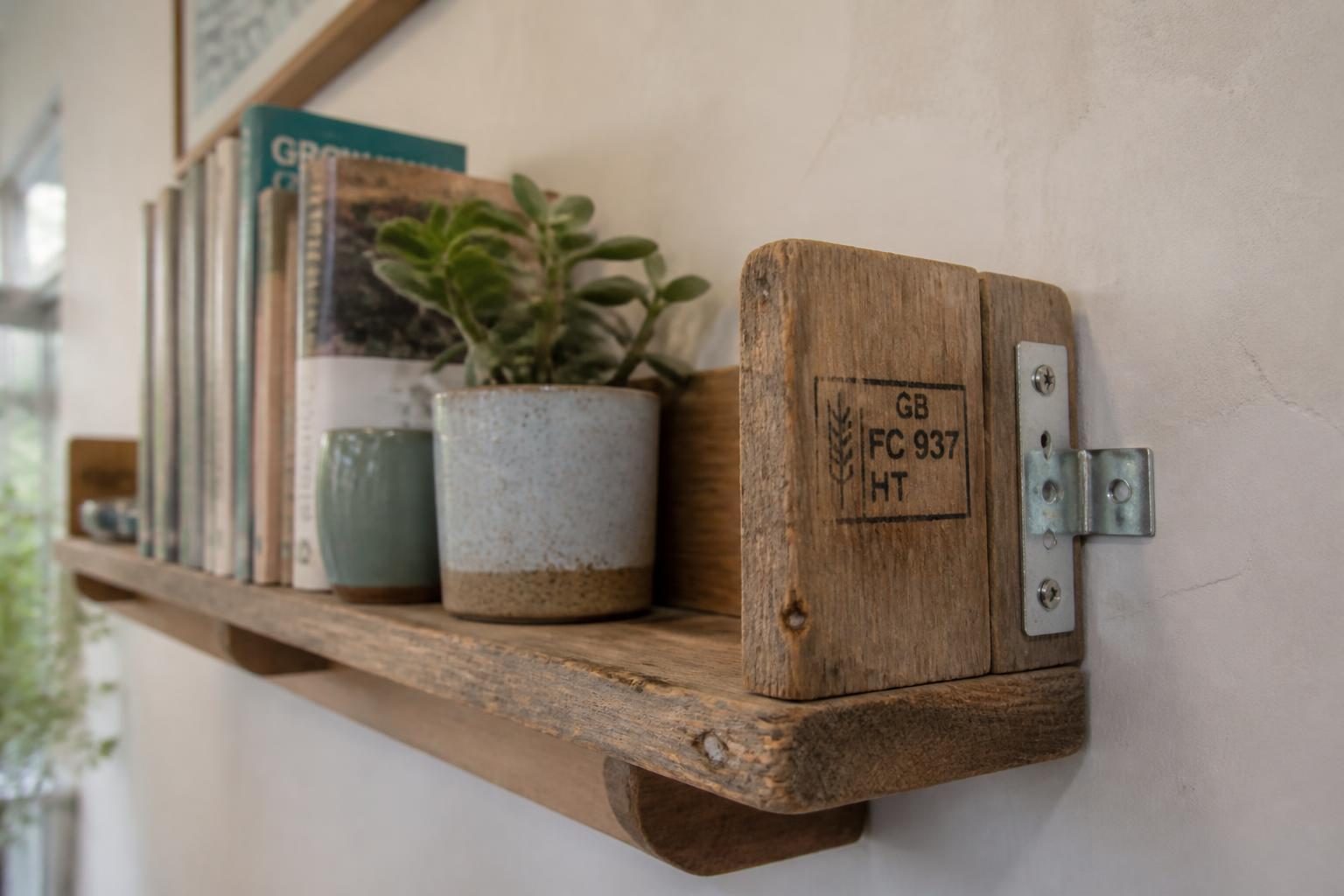 Étagère murale en bois de palette fixée au mur, livres et plantes, marquage HT visible sur le bois